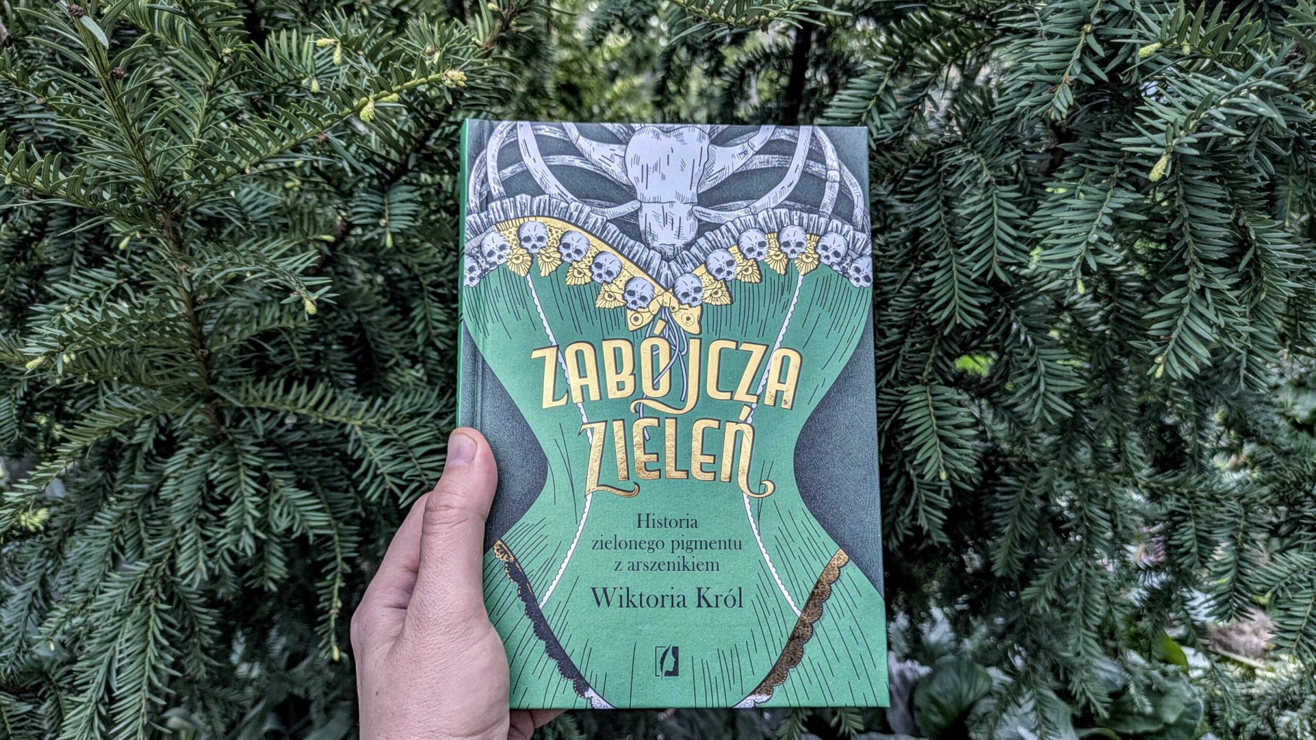 książka "Zabójcza zieleń" na tle roślin